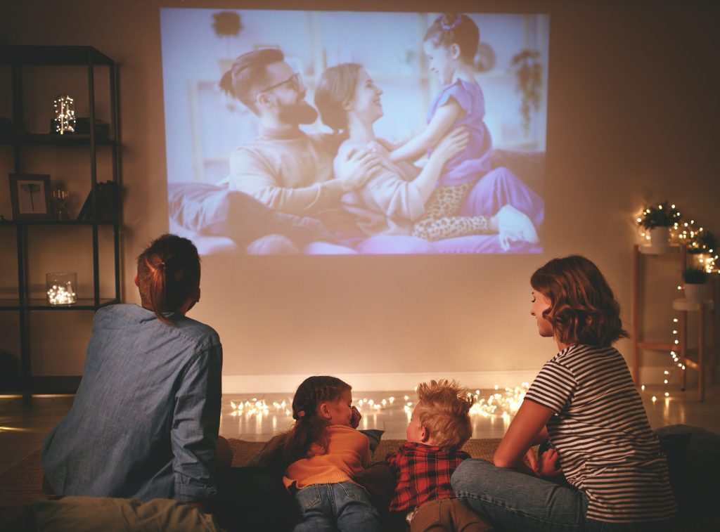 family mother father and children watching projector, TV, movies with popcorn in evening at home